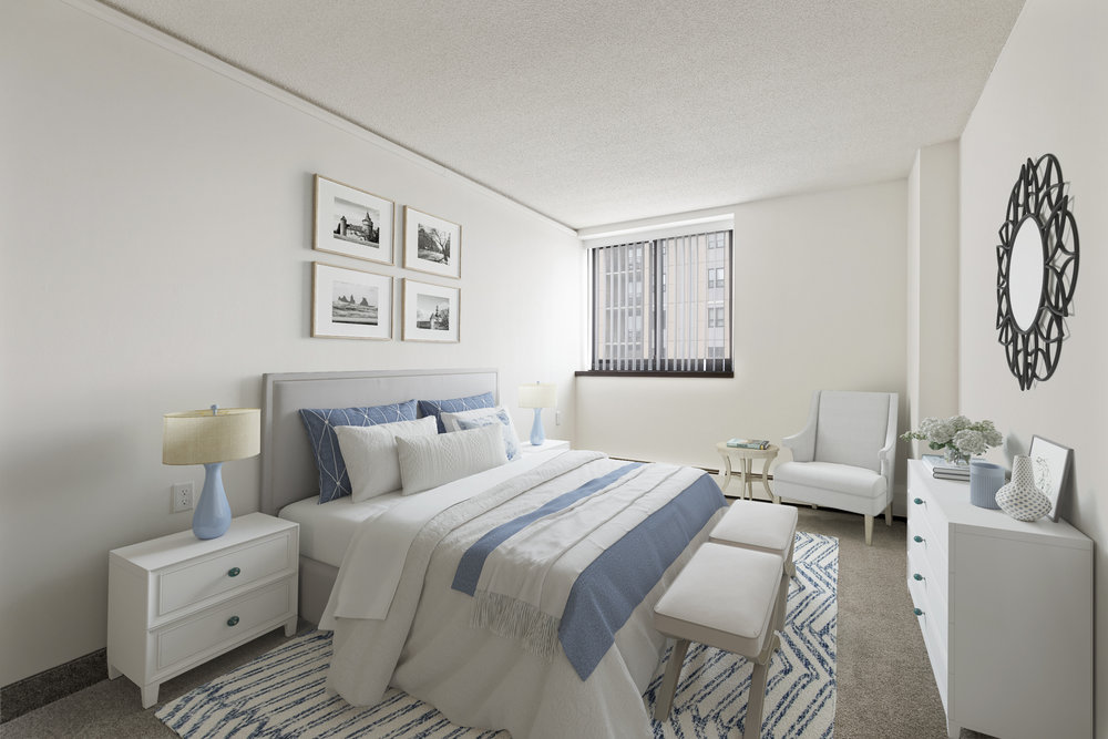 Bright, modern bedroom with a large bed, blue and white decor, dresser, and window showing city buildings.