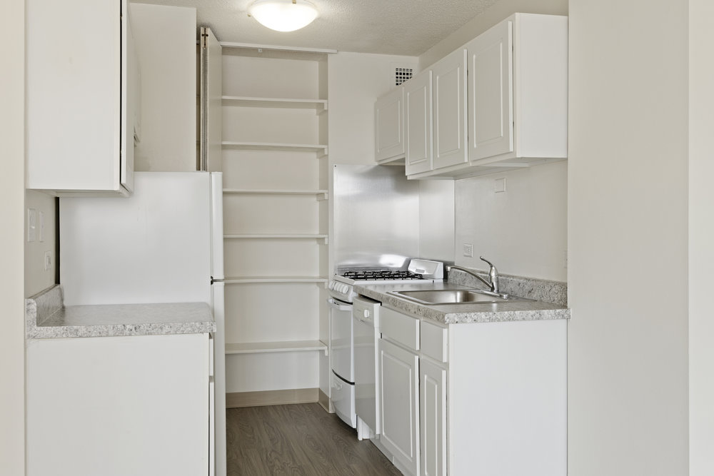 Narrow kitchen with white cabinets, a gas stove, sink, open shelves, and marble countertops.