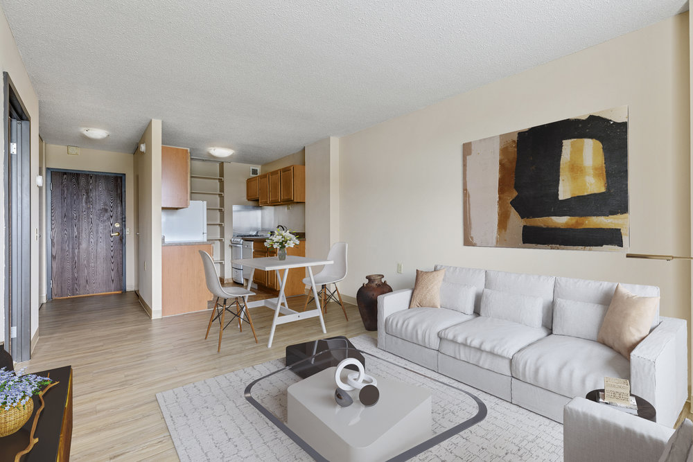Modern living room with white sofa, abstract art, dining table, and open kitchen with wooden cabinets.